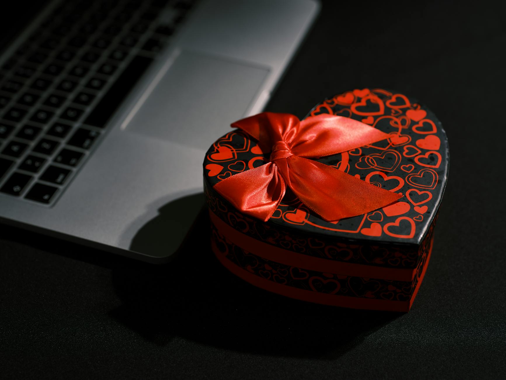 Czarne pudełko prezentowe w kształcie serca obok laptopa na ciemnym biurku