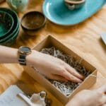 Kobieta pakuje kartonowe pudełko z wypełnieniem na drewnianym biurku