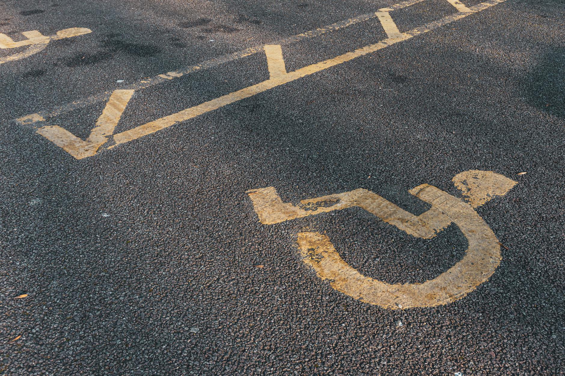 Jak zaplanować dostępne wakacje z osobą z niepełnosprawnością krok po kroku Symbol wózka inwalidzkiego namalowany na asfalcie parkingu